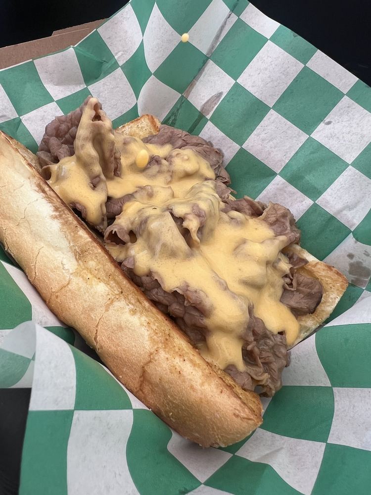 A cheesy Italian beef on a toasted roll over green-checkered paper